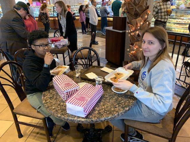 two students at a table in a bakery, eating dessert